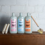 Bio-D 750ml pink grapefruit, fragrance free and mandarin bottles of washing up liquid standing on a wooden surface next to cleaning products. All 3 fragrances are available at Babipur