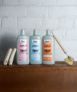 Bio-D 750ml pink grapefruit, fragrance free and mandarin bottles of washing up liquid standing on a wooden surface next to cleaning products. All 3 fragrances are available at Babipur