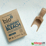Bio-D Laundry Bleach cardboard box next to loose white powder with blue flecks and a wooden scoop, showing the powdered texture and Allergy UK Friendly Product logo.