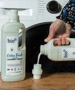 Bio-D cotton fresh non bio laundry liquid being poured in a cap with a washing machine in the background.