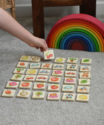 A child picking a tile from the Bajo Wooden Tiles Memory Game. The tile has an illustration of a cherry on it. All the tiles from the set have been laid out and are showing the different illustration. These heirloom quality toys by Bajo are part of a wide range of wooden toys available here at Babipur. 