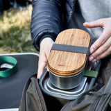 Adult hand putting a Black+Blum stainless steel leakproof bento box in a backpack