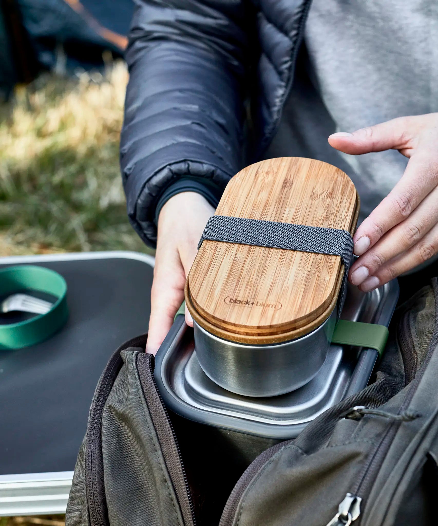 Adult hand putting a Black+Blum stainless steel leakproof bento box in a backpack