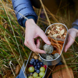 Adult hand reaching into a Black+Blum stainless steel leakproof bento box filled with food