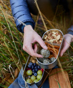 Adult hand reaching into a Black+Blum stainless steel leakproof bento box filled with food
