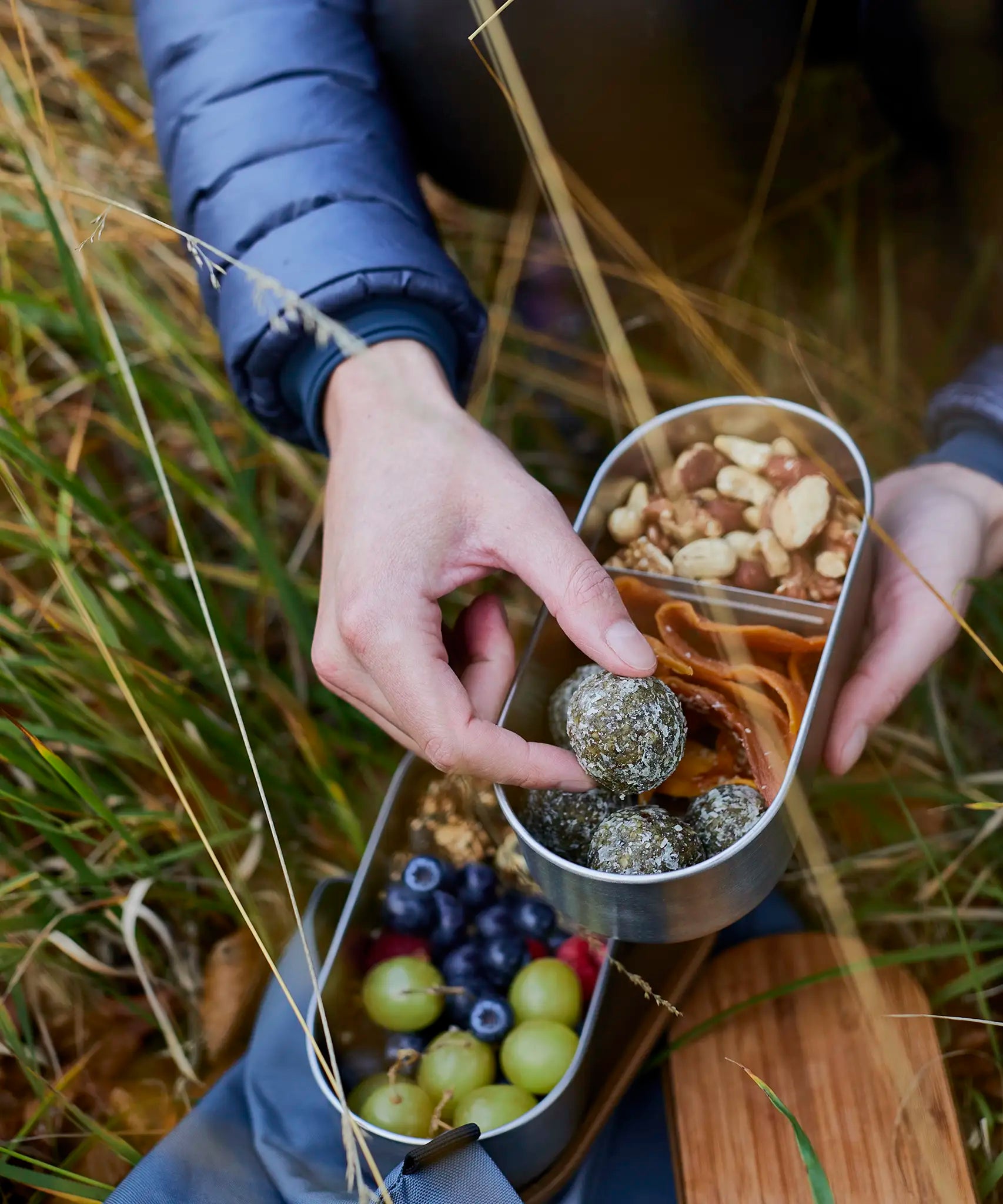 Adult hand reaching into a Black+Blum stainless steel leakproof bento box filled with food