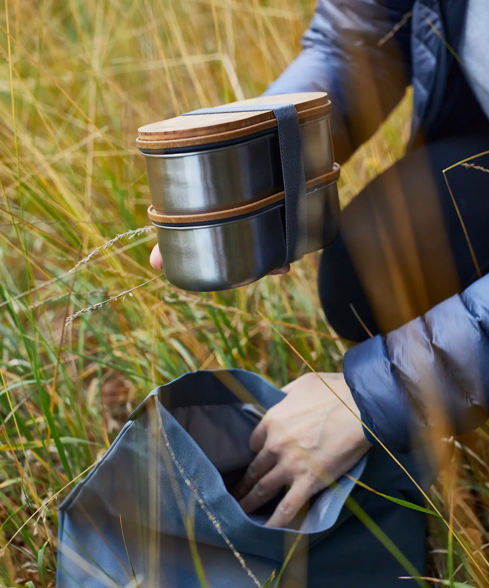 Adult putting in two Black+Blum stainless steel leakproof bento lunchboxes in a backpack