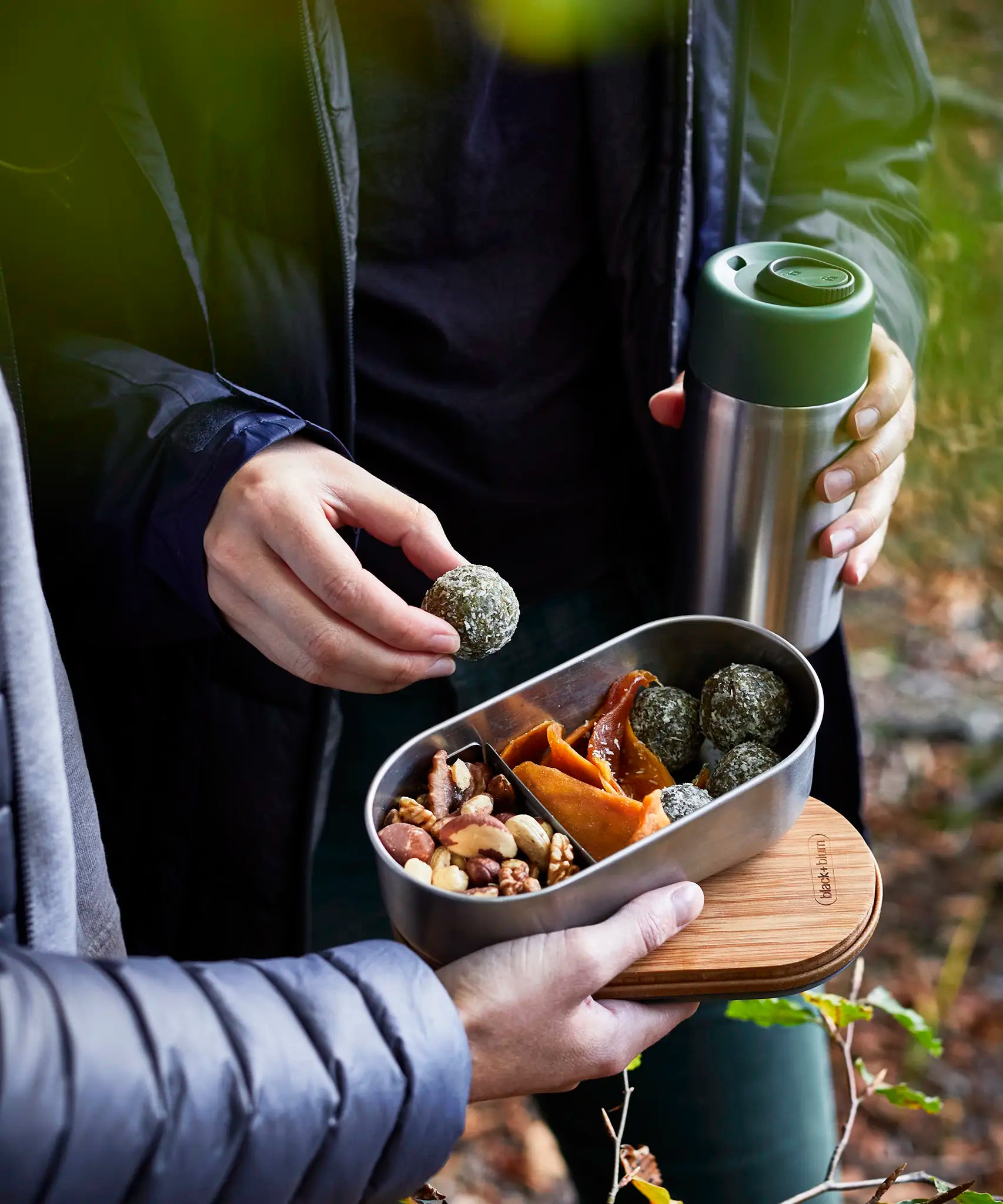 Adult picking up food from a Black+Blum stainless steel leakproof bento box held by another person