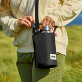 Adult carrying a Black + Blum insulated  bottle bag in black over the shoulder showing a flask and mobile phone inside