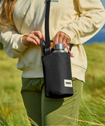 Adult carrying a Black + Blum insulated  bottle bag in black over the shoulder showing a flask and mobile phone inside