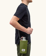 Adult carrying a Black + Blum insulated  bottle bag in moss green over the shoulder showing a flask inside