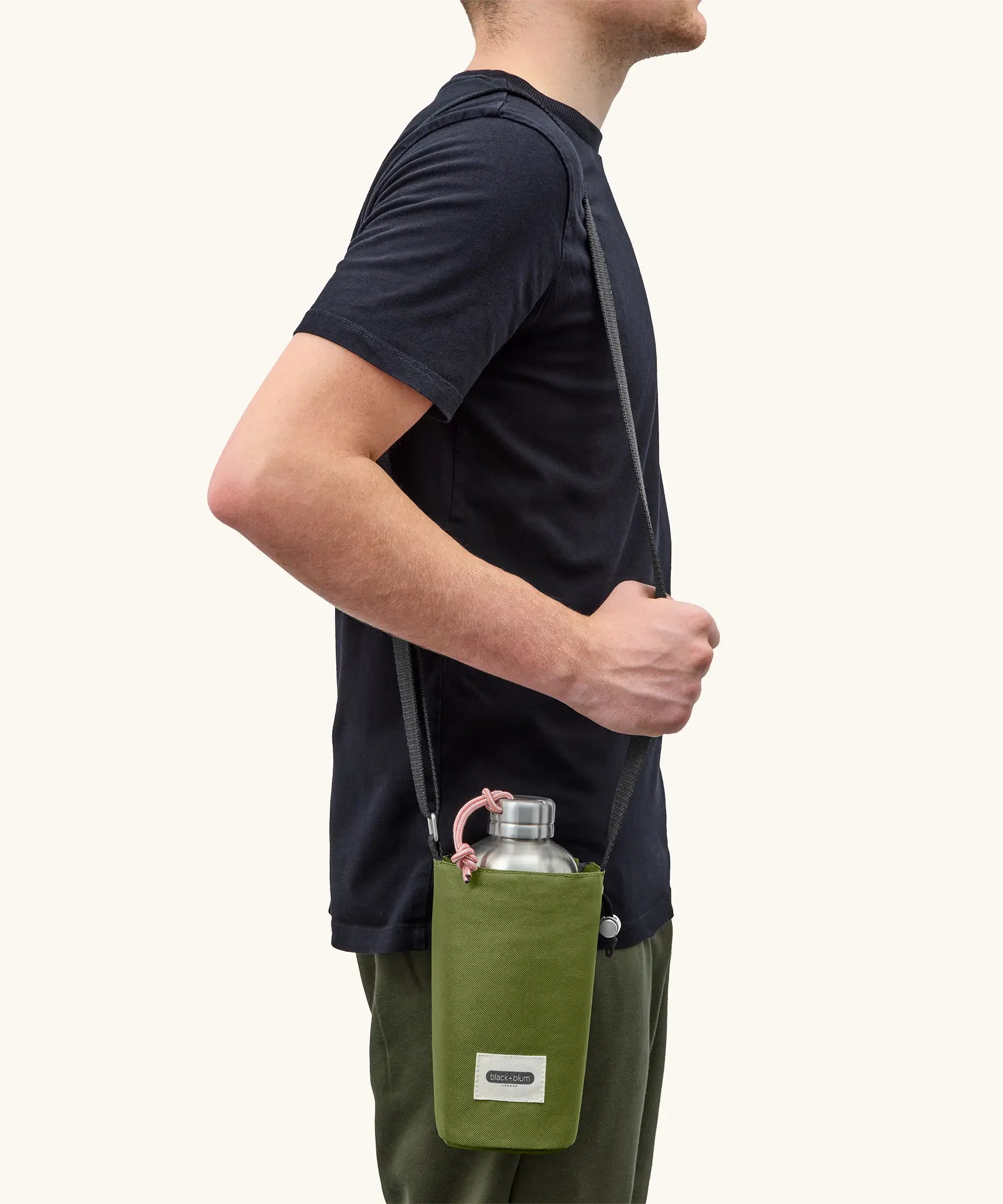 Adult carrying a Black + Blum insulated  bottle bag in moss green over the shoulder showing a flask inside
