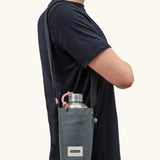 Adult carrying a Black + Blum insulated  bottle bag in slate blue over the shoulder showing a flask inside