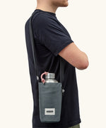 Adult carrying a Black + Blum insulated  bottle bag in slate blue over the shoulder showing a flask inside