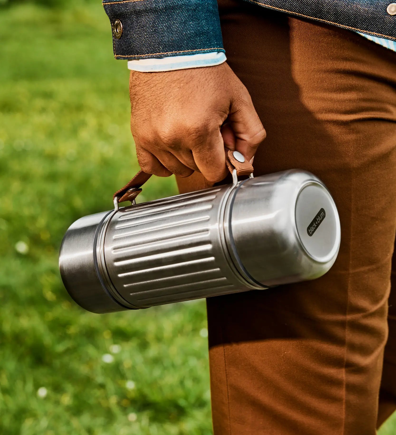 Adult carrying a Black+Blum 1litre stainless steel insulated explorer duo flask by the nylon carry handle