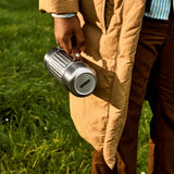 Man holding a Black+Blum 1litre stainless steel insulated explorer duo flask in a grassy field