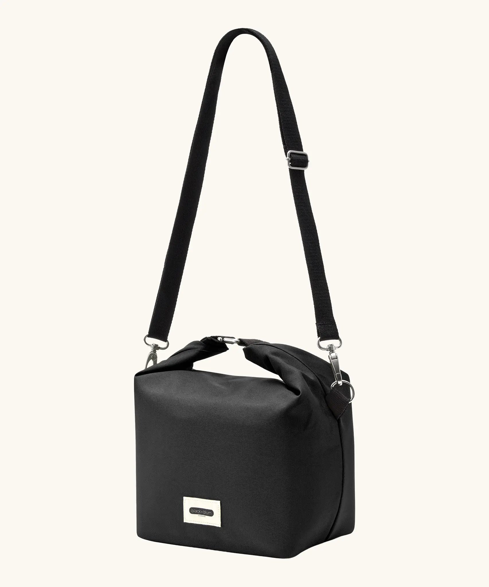 A full Black+Blum 10 litres insulated and roll top lunch bag in black showing the carry strap hooked on the side loops