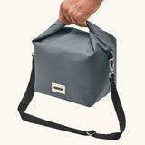 Adult hand carrying the Black+Blum 10 litres insulated lunch bag in slate grey by the roll top handle