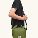 Adult carrying the Black+Blum 10 litres insulated roll top lunch bag in moss green over the shoulder
