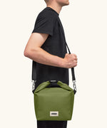 Adult carrying the Black+Blum 10 litres insulated roll top lunch bag in moss green over the shoulder
