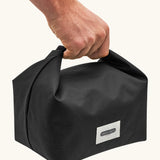 Adult hand carrying a Black+Blum 7 litres insulated and water repellent roll top lunch bag in black 