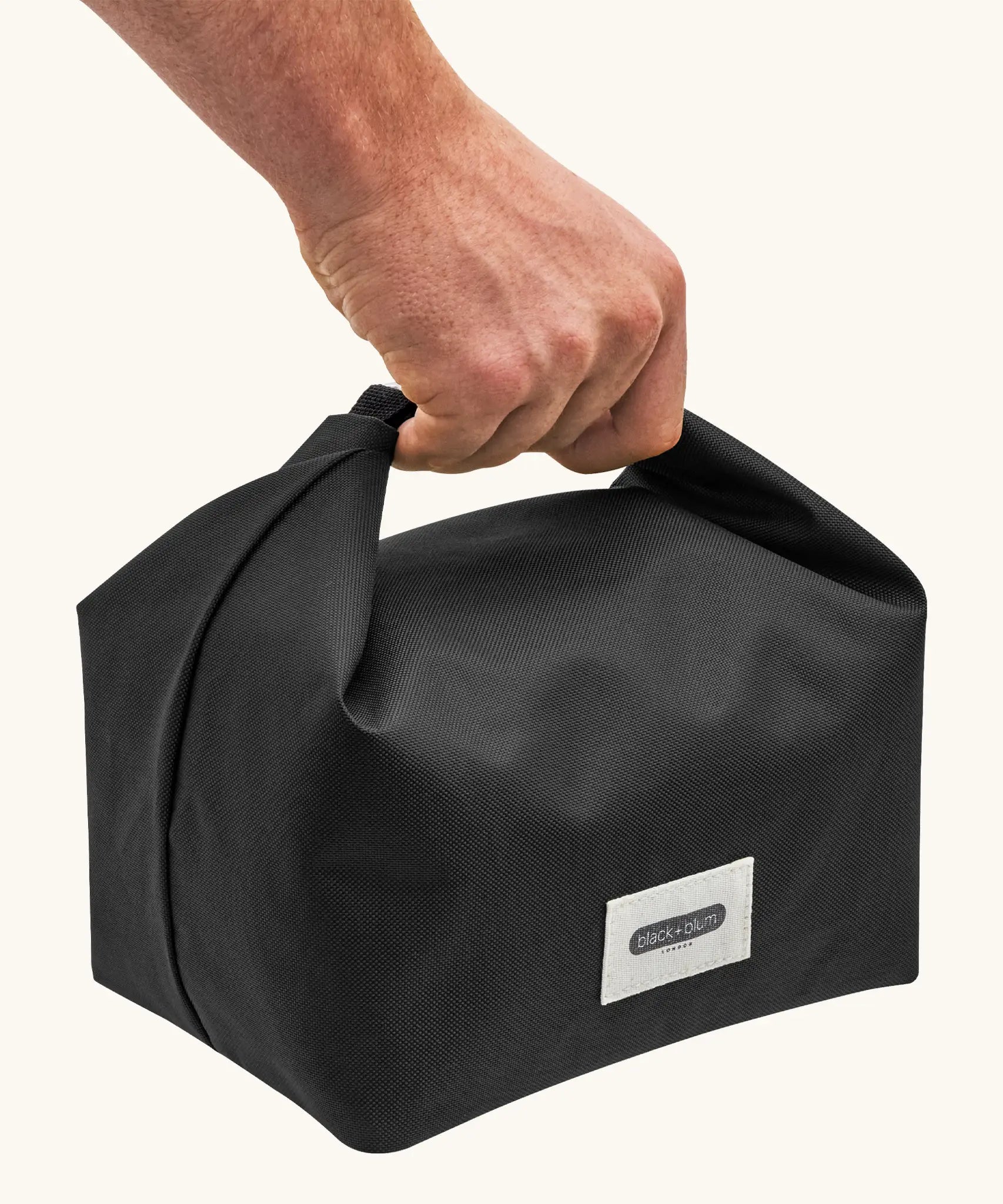 Adult hand carrying a Black+Blum 7 litres insulated and water repellent roll top lunch bag in black 