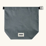 A slate blue Black+Blum water repellent roll top lunch bag laid flat showing the hook buckle and brand patch on the bottom