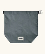 A slate blue Black+Blum water repellent roll top lunch bag laid flat showing the hook buckle and brand patch on the bottom