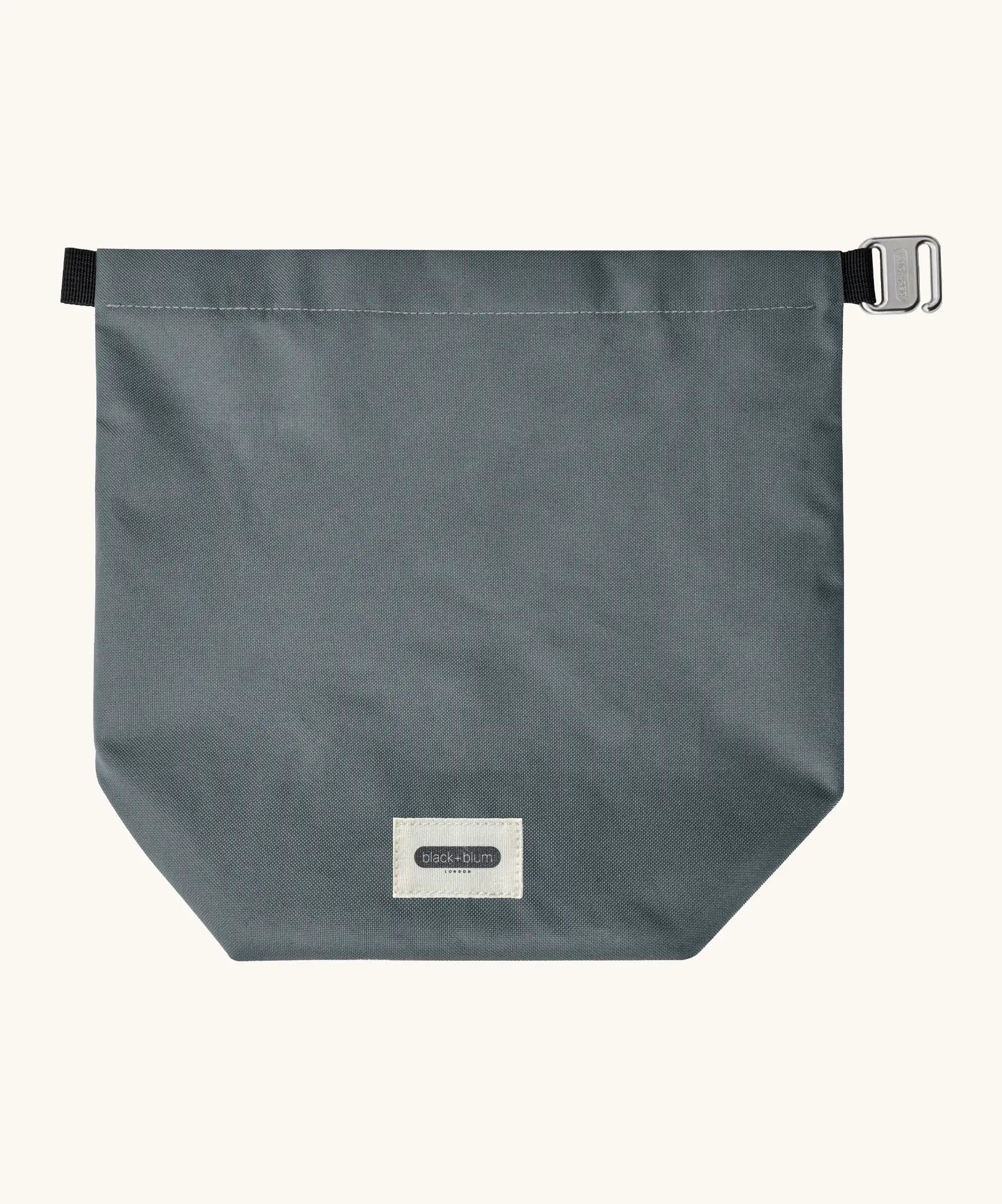 A slate blue Black+Blum water repellent roll top lunch bag laid flat showing the hook buckle and brand patch on the bottom