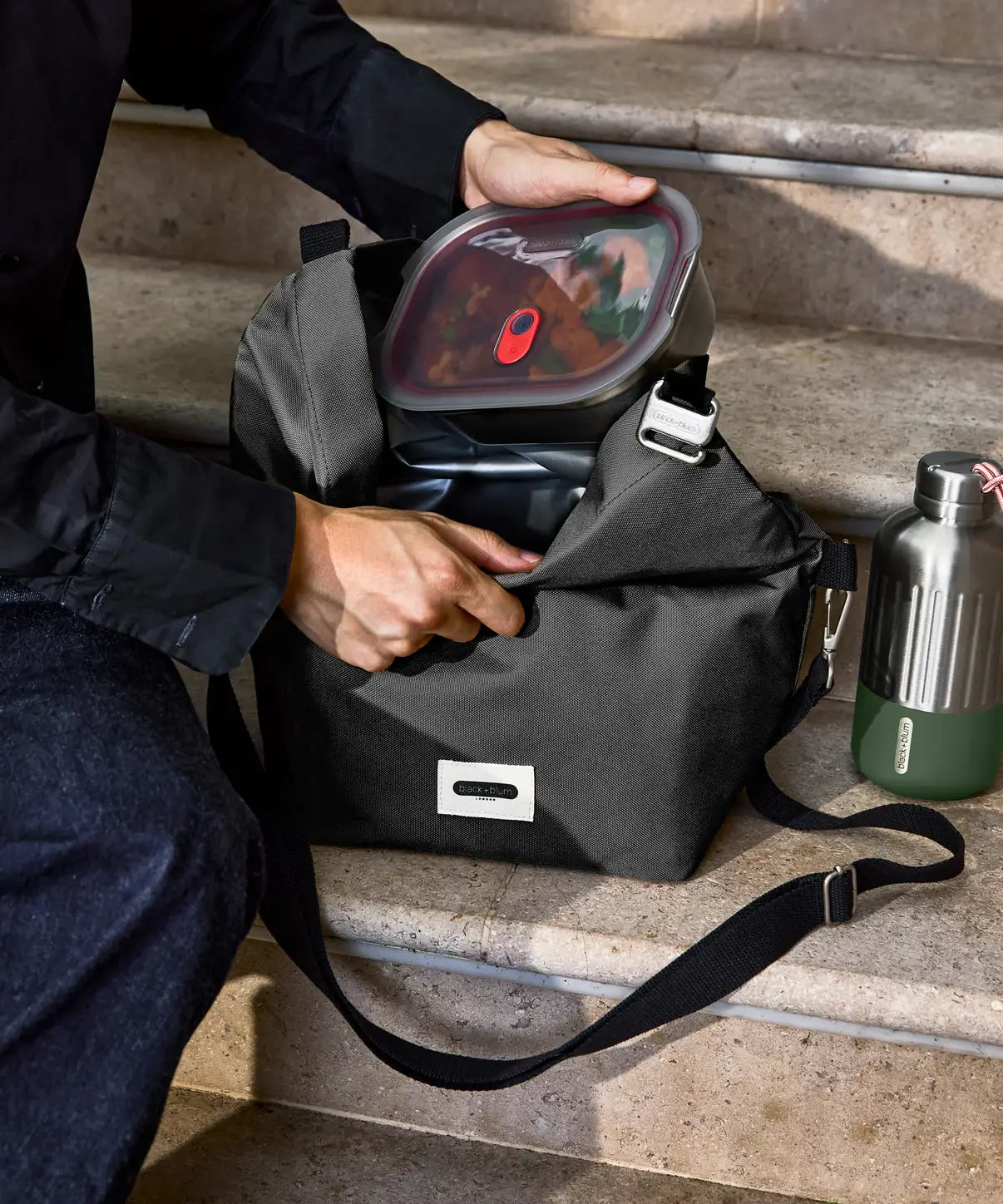Adult packing away a lunchbox inside a Black + Blum black insulated lunch bag