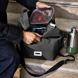 Adult packing away a lunchbox inside a Black + Blum black insulated lunch bag