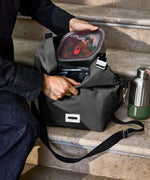 Adult packing away a lunchbox inside a Black + Blum black insulated lunch bag