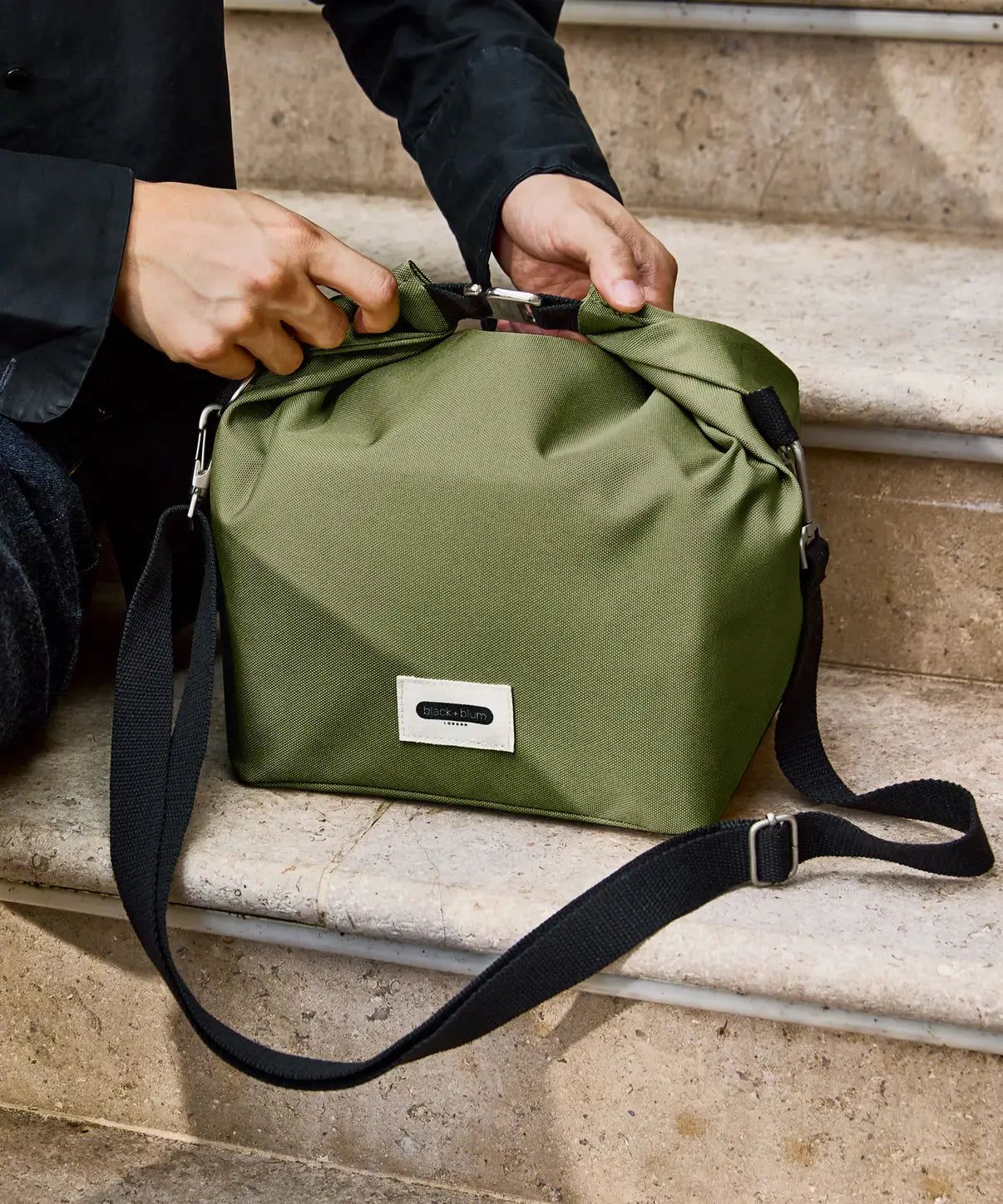 Adult hooking the buckle on the roll top handle on the Black + Blum moss green insulated lunchbag