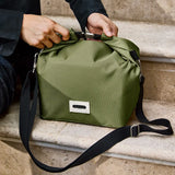 Adult hooking the buckle on the roll top handle on the Black + Blum moss green insulated lunchbag