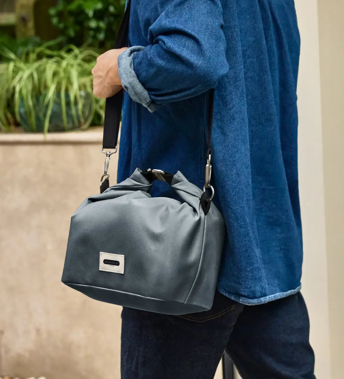 Adult carrying the Black+Blum 10 litres insulated roll top lunch bag in slate blue  over the shoulder with the carry strap