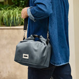 Adult carrying the Black+Blum 10 litres insulated roll top lunch bag in slate blue  over the shoulder with the carry strap