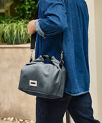 Adult carrying the Black+Blum 10 litres insulated roll top lunch bag in slate blue  over the shoulder with the carry strap