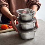 A adult standing by a stone worktop with the 3 different sized Black + Blum stainless steel lunchbox stacked on top of eachother