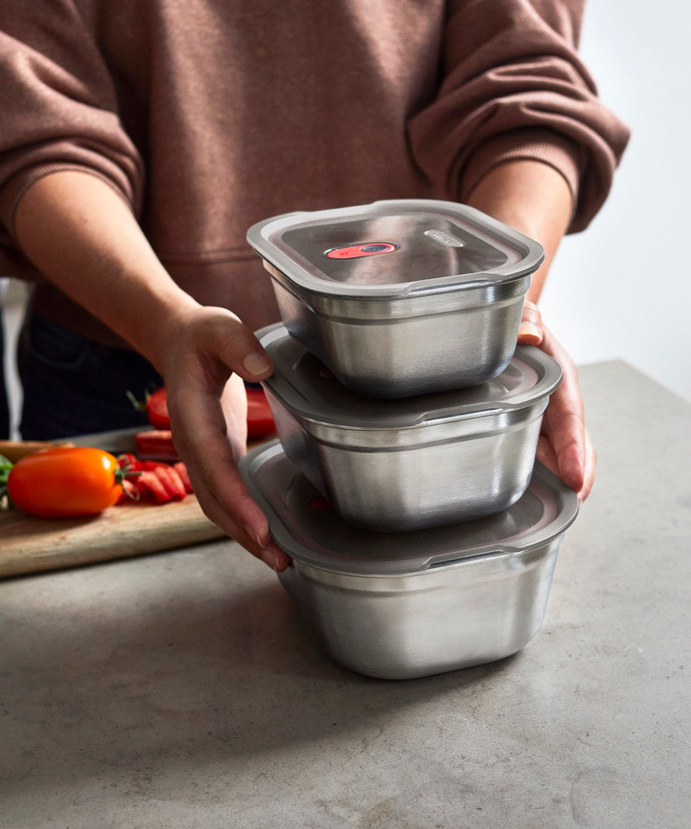 A adult standing by a stone worktop with the 3 different sized Black + Blum stainless steel lunchbox stacked on top of eachother