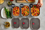 A top down view of the 3 diferent sized Black + Blum stainless steel lunch boxes next to eachother on a stone worktop with food inside and the grey lids next to each lunchbox