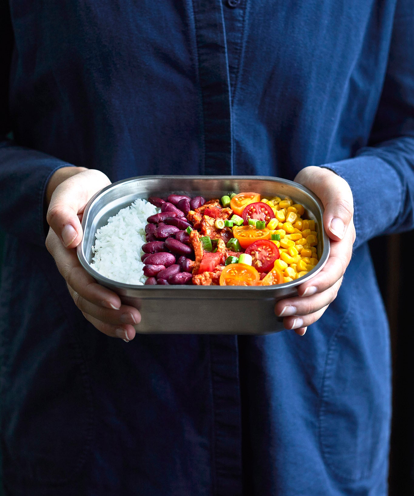 A adult standing and holding the Black + Blum stainless steel lunchbox with food inside.
