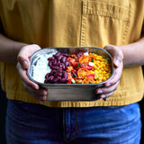 A adult standing and holding the 600ml Black + Blum stainless steel lunchbox with food inside.