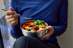 A close up of an adult eating from  a small Black + Blum stainless steel bowl 