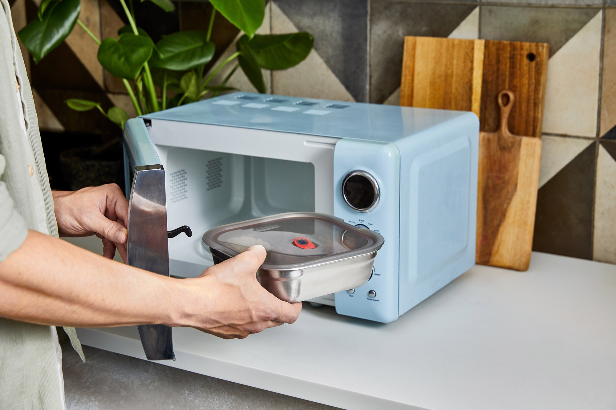An adult putting a Black + Blum
stainless steel microwave safe leakproof lunchbox inside a microwave for cooking. Lunchbox is available at Babipur.