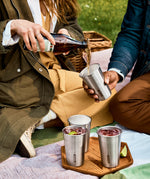 A close up of a couple of adults having a picnic and pouring drink into the Black + Blum stainless steel cups 