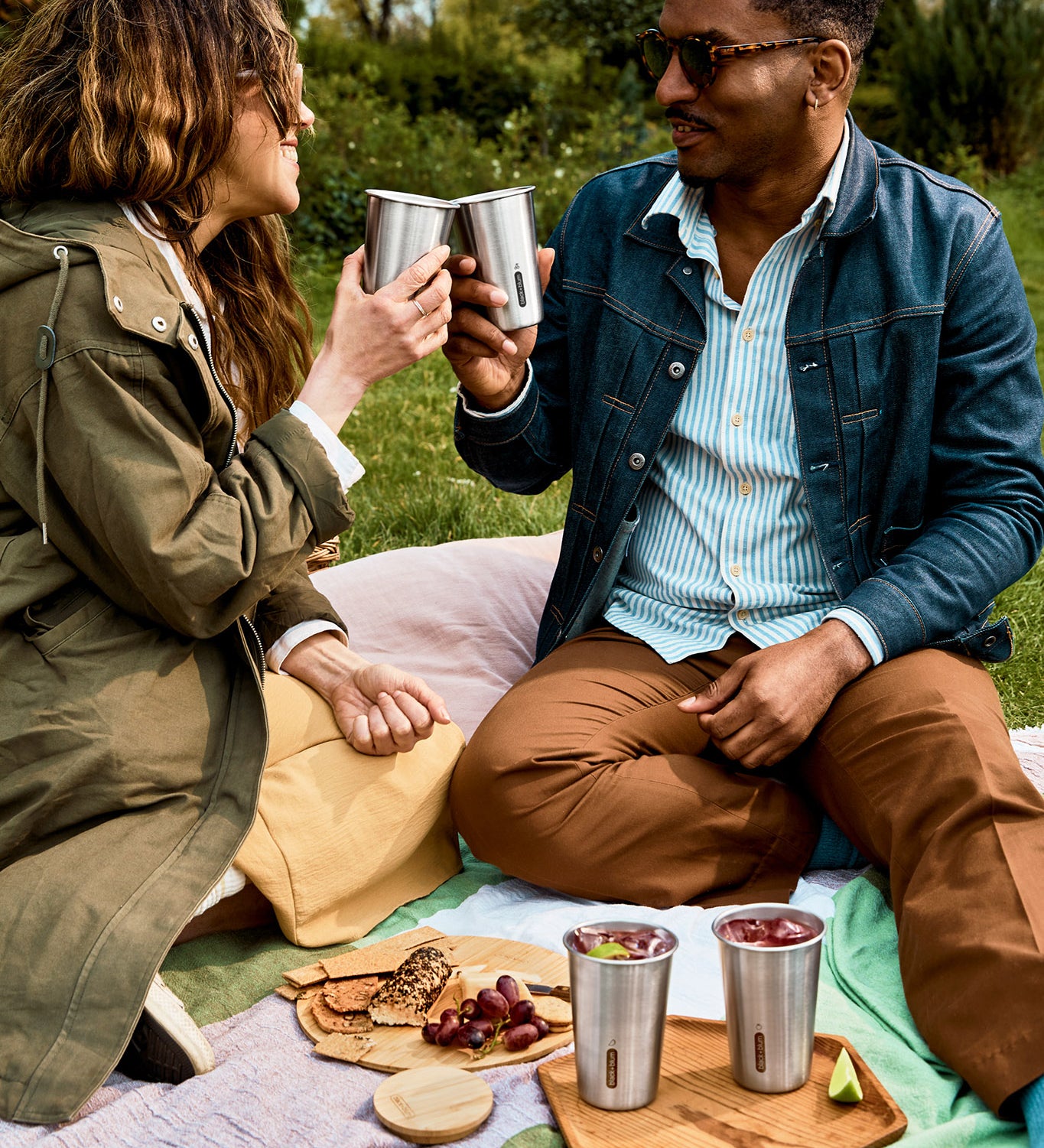 A couple of adults having a picnic outside and holding the Black + Blum stainless steel cups 