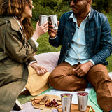 A couple of adults having a picnic outside and holding the Black + Blum stainless steel cups 