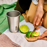 A person slicing a lime on the bamboo lid from the black and blum stainless steel cup and lid set. 