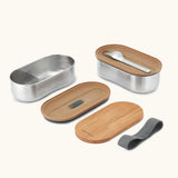 An open Black+Blum 500ml stainless steel leakproof bento box showing a fork and bamboo lid/chopping board