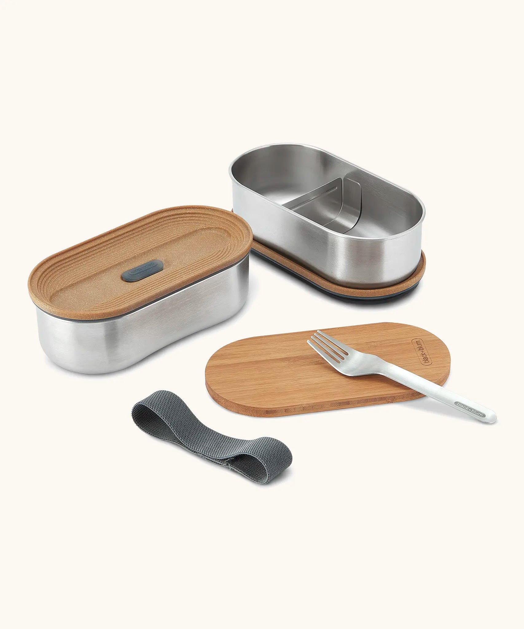 An open Black+Blum stainless steel leakproof bento lunchbox showing a fork and bamboo lid/chopping board